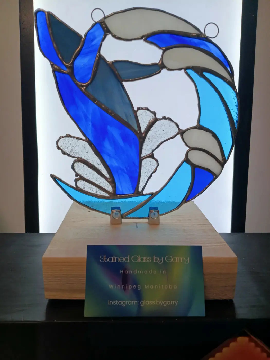 Handmade stained glass breaching whale artwork with stylized blue and white wave design set in wooden base