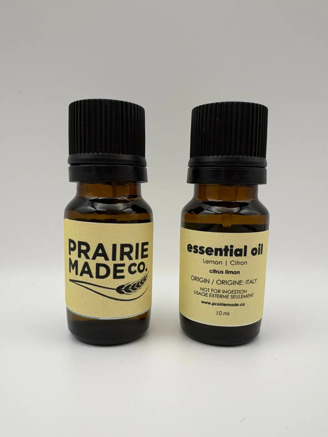 Two amber glass bottles with black caps labeled prairie made.co and essential oil lemon from italy for natural skincare canada