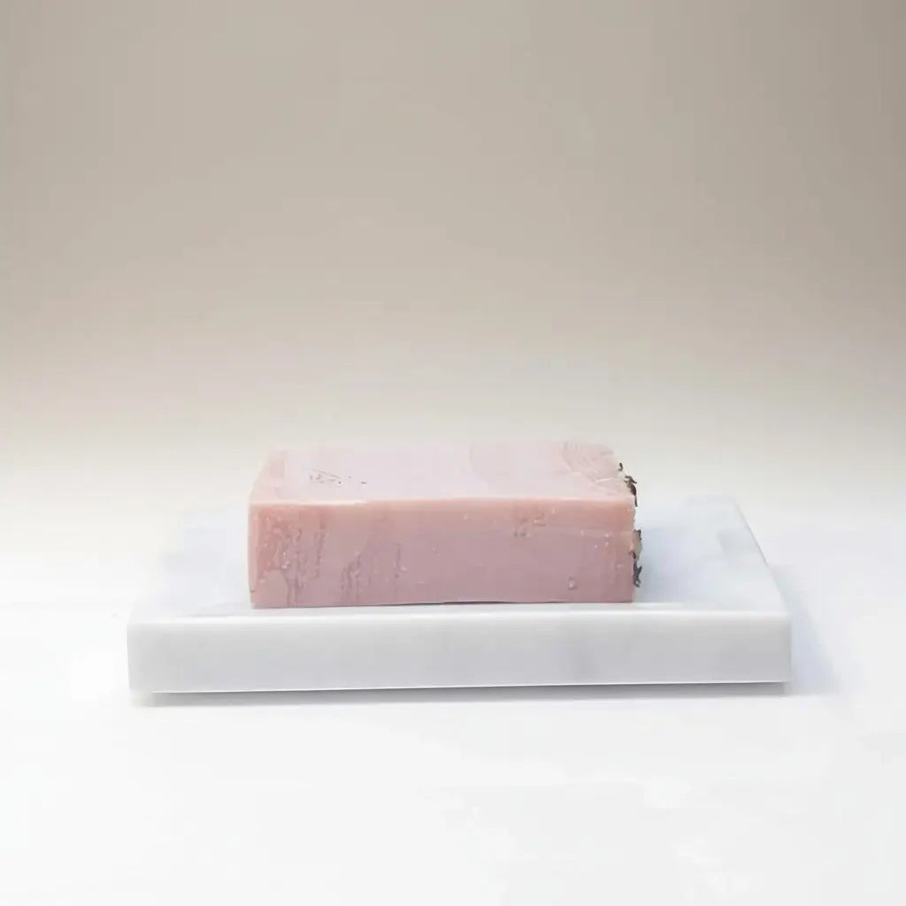 A rectangular pink fruity floral fiesta soap bar with subtle marbling on a white marble soap dish by rocky mountain soap