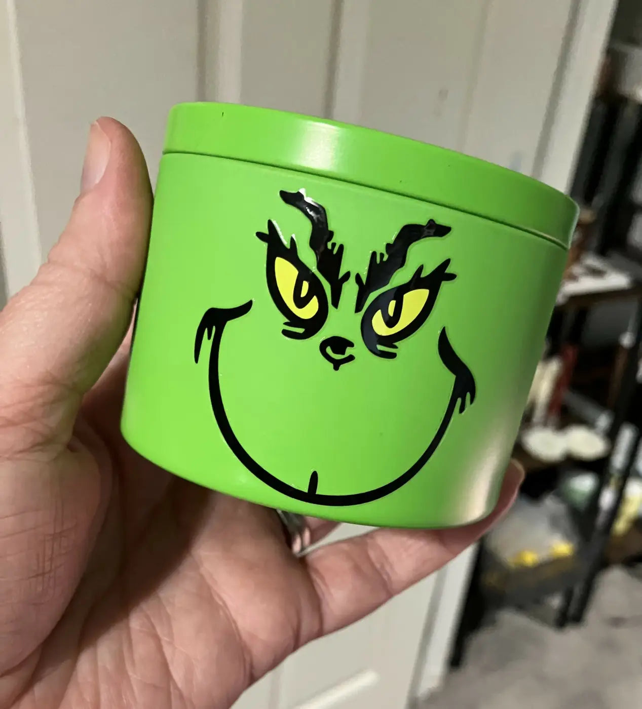 Bright green specialty character candle tin featuring a black and yellow grinch face with clean-burning holiday soy wax