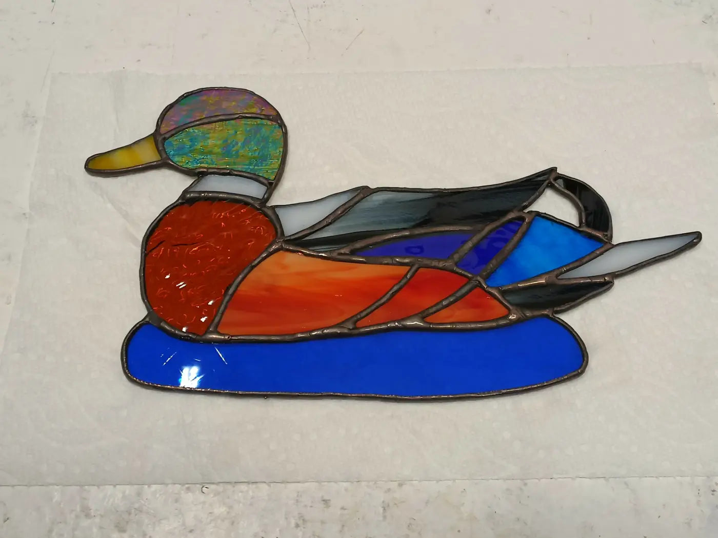 A handmade stained glass duck with a multicolored head, orange body, and blue wings multi colored craft