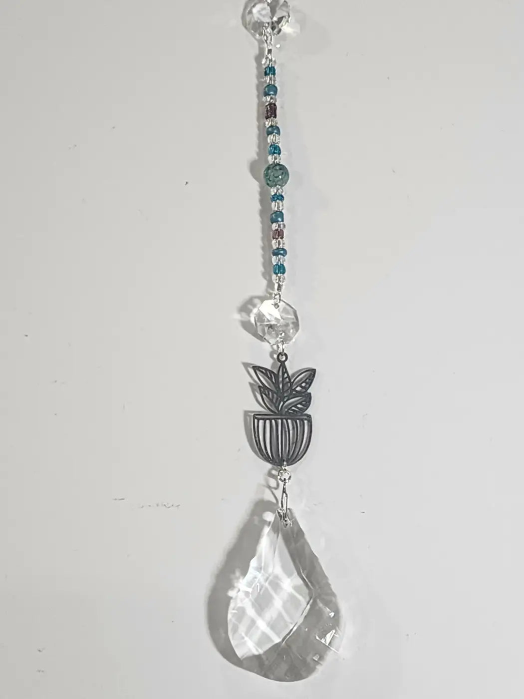Plant long suncatcher with clear faceted crystal pendant, teal and silver beads, and dark metal planter charm as iridescent ornament