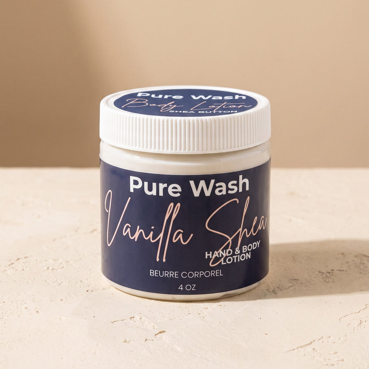 Pure Wash Vanilla Shea hand and body lotion in a 4 oz white jar on a textured beige surface.