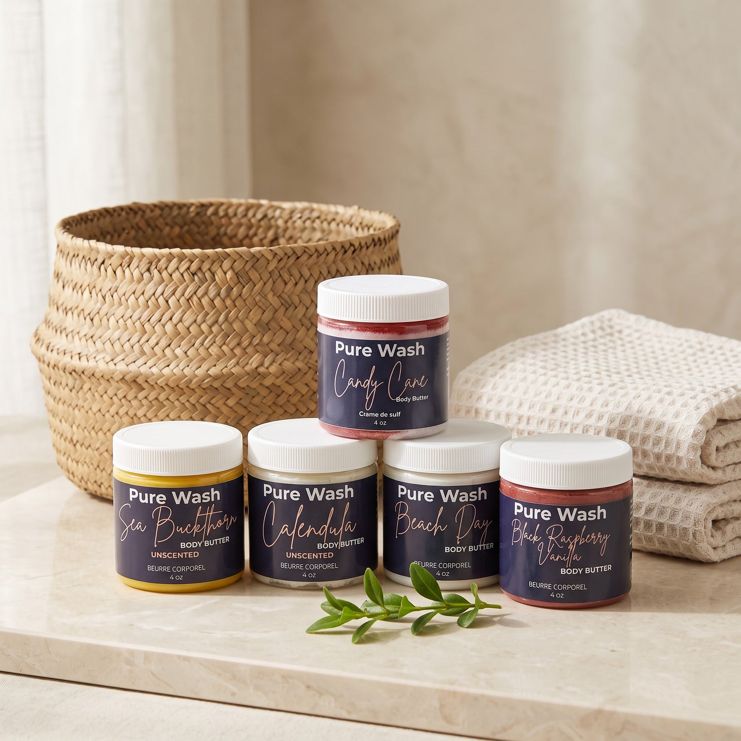 Pure Wash whipped body butter jars in various scents displayed on a marble surface with a woven basket and towel.