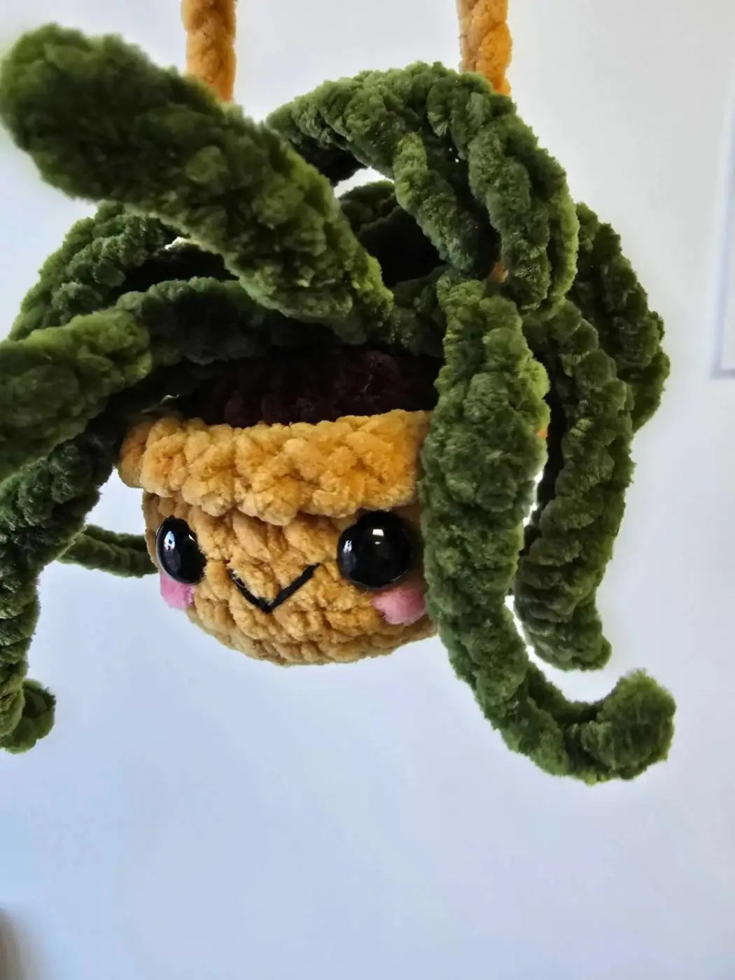 A charming green and yellow handmade crocheted spider plants holder with fluffy yarn tendrils and pink cheeks perfect for pure wash use