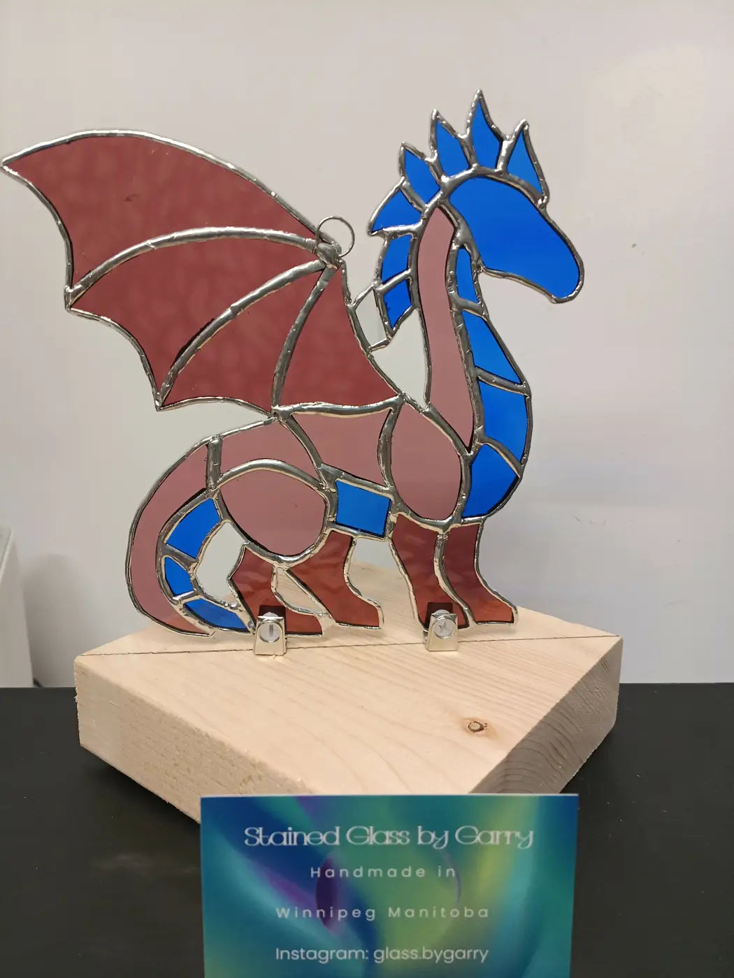 Whimsical dragon handmade stained glass dragon with blue and rose panels outlined in silver on wooden base