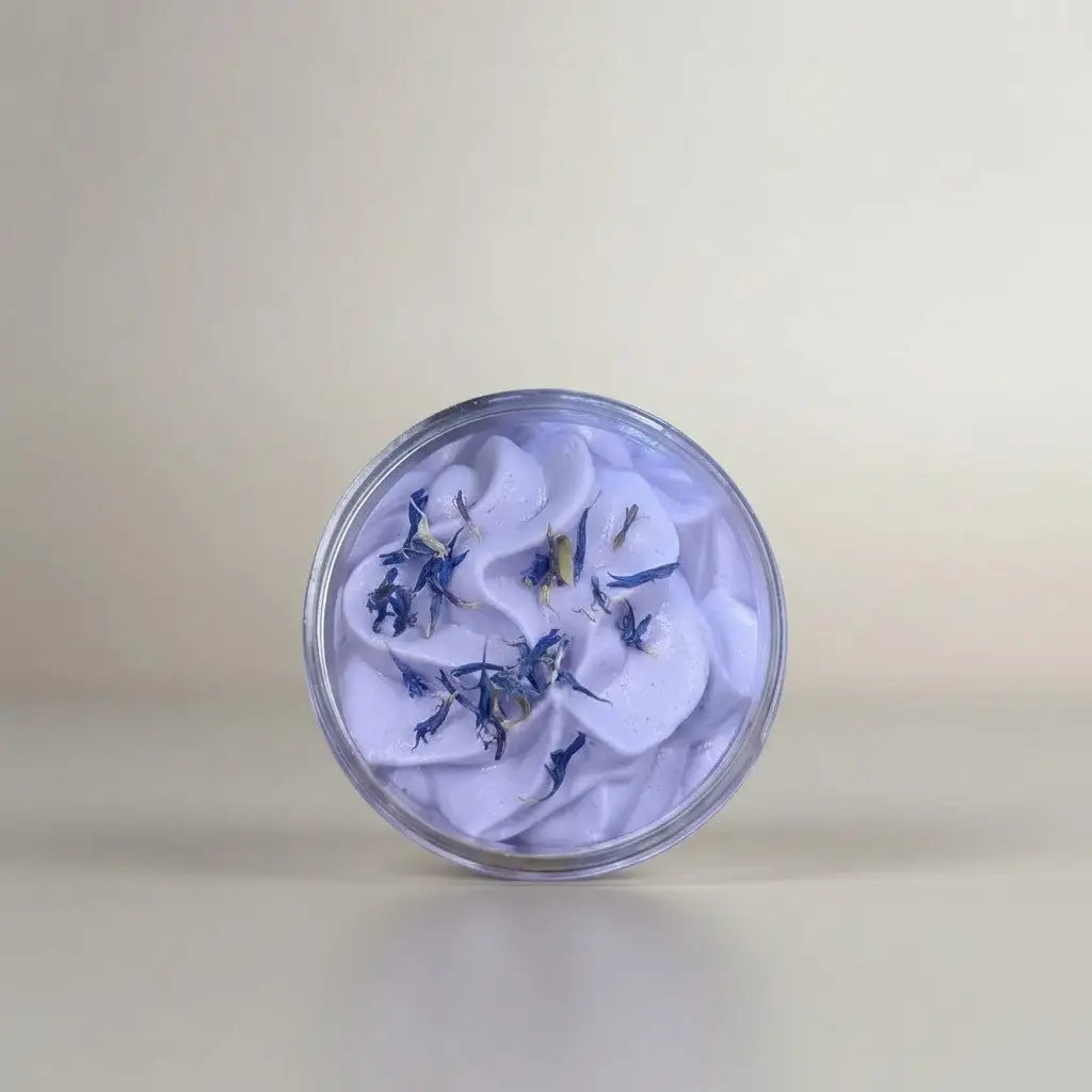 A clear glass jar of lavender whipped soap with dried blue and yellow petals for a gentle cleanser for sensitive skin