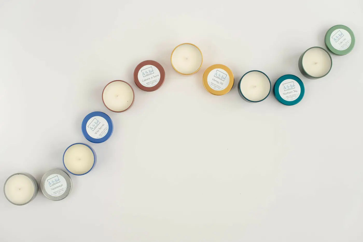 A collection of mini soy wax candle tin assorted colorful metal tins with white wax center and branded labels for gifting