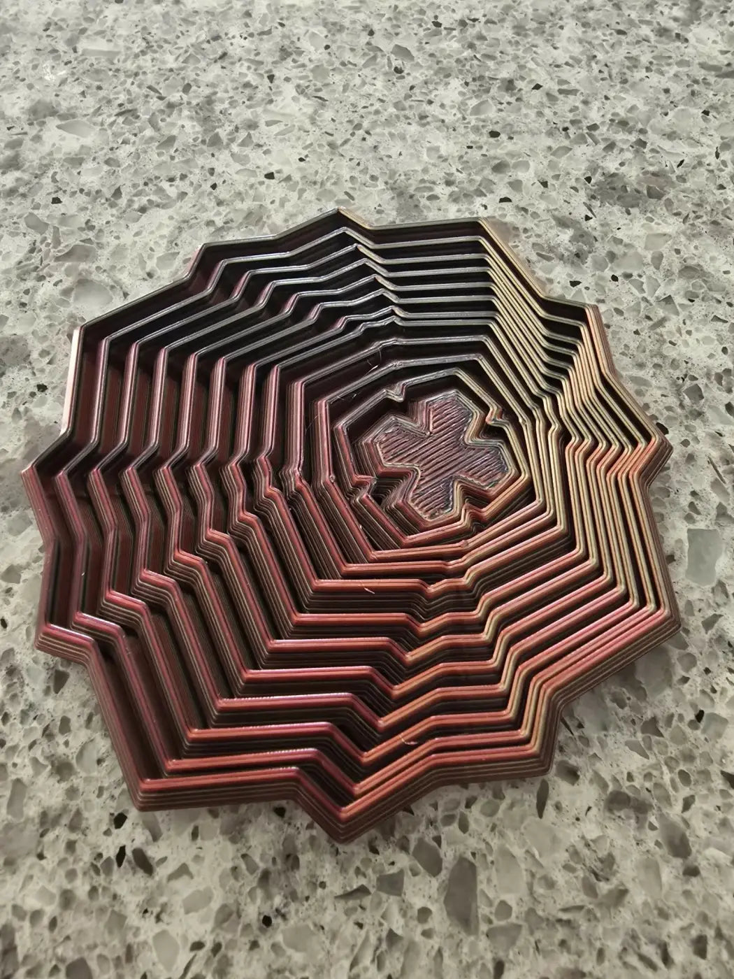 A multi-layered octagonal 3d printed fidget star with zigzag edges and coppery red concentric rings wooden sensory toy