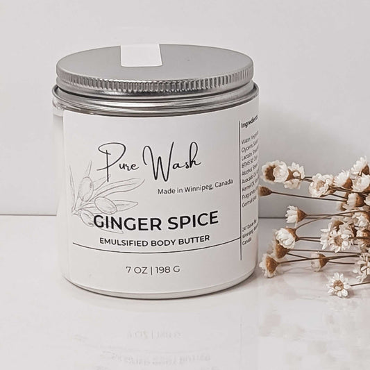 A jar of CG Pure Wash's Ginger Spice Emulsified Body Butter sitting on a wooden table with ginger and cinnamon sticks