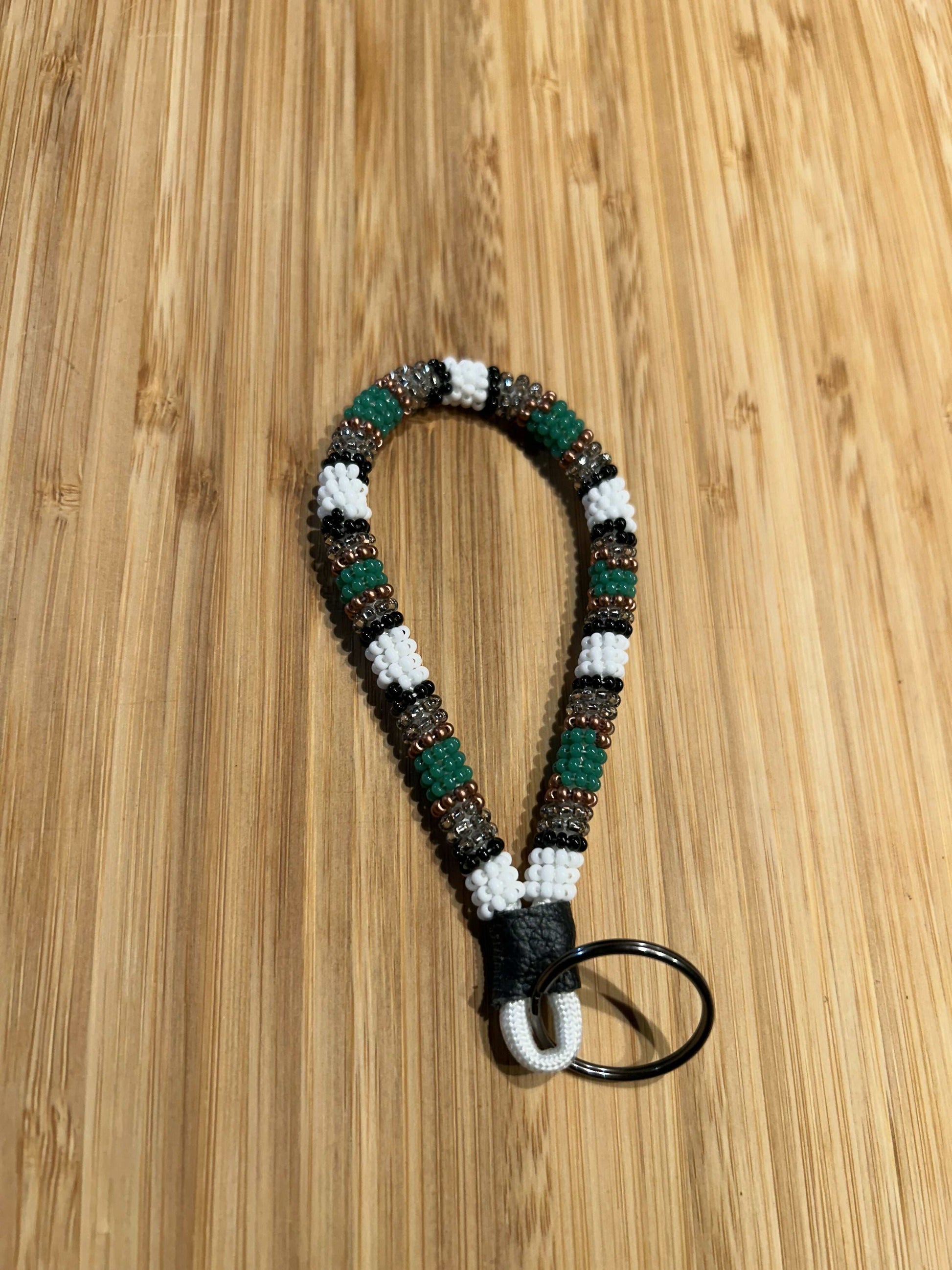 HERA Beaded Mini Keychain with bold rich colors, leather strap, and key ring on wooden background.