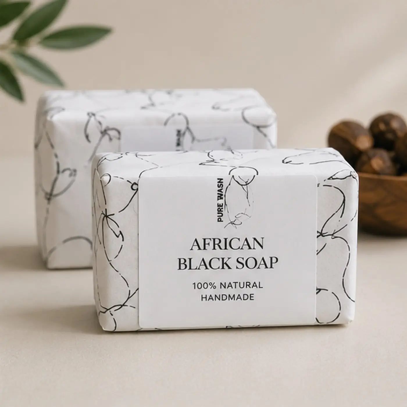 A rectangular bar of african black soap wrapped in white paper with black line art labeled pure wash 100% natural handmade raw african black soap natural