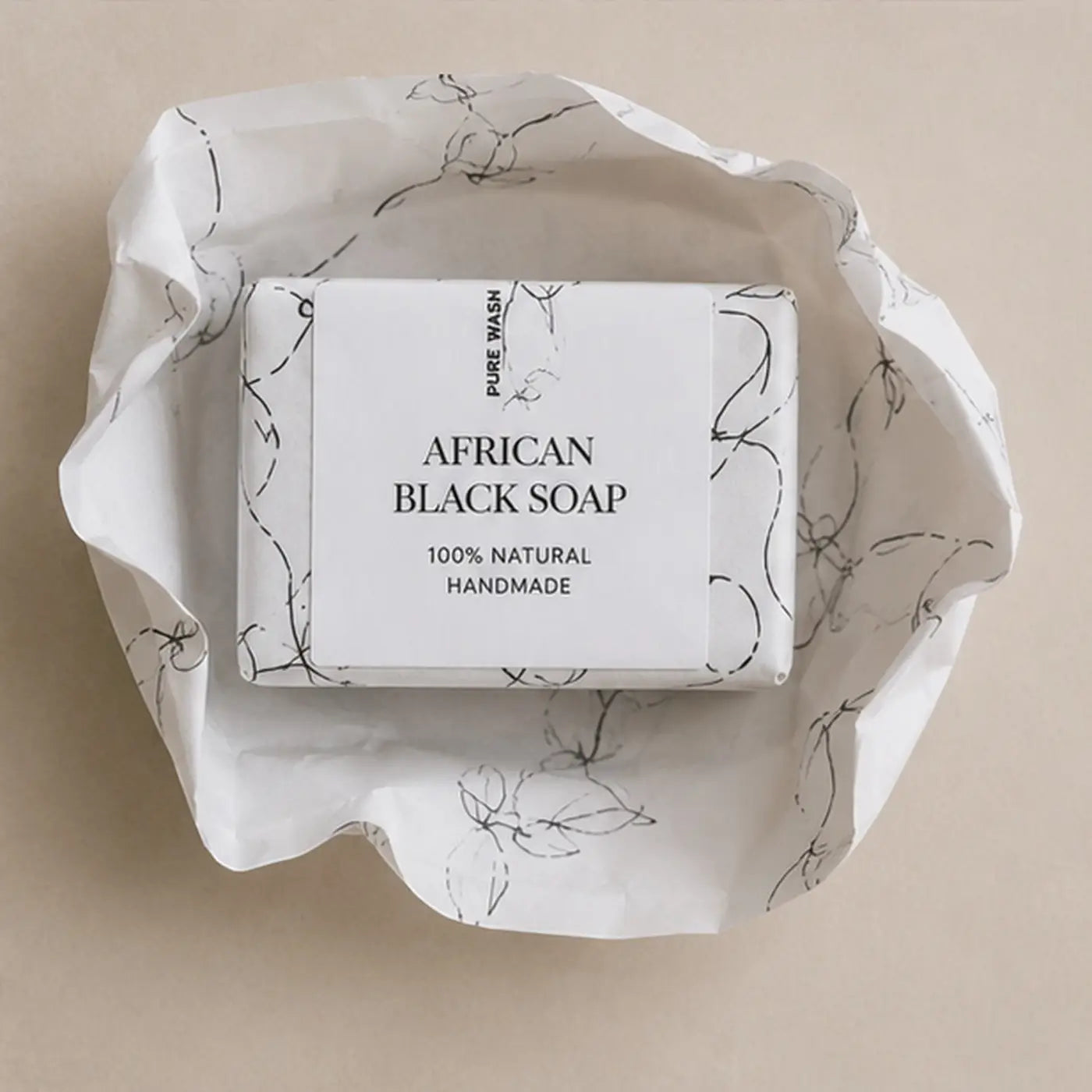 A rectangular bar of african black soap wrapped in white paper with black line art labeled pure wash 100 percent natural handmade for raw african black soap natural benefits and acne care