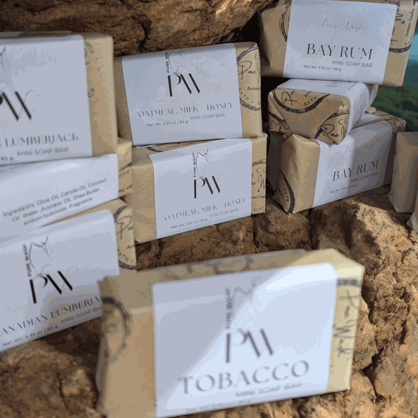Mini soap bars displayed on natural rocks with various scents like Bay Rum and Tobacco, showcasing eco-friendly packaging.