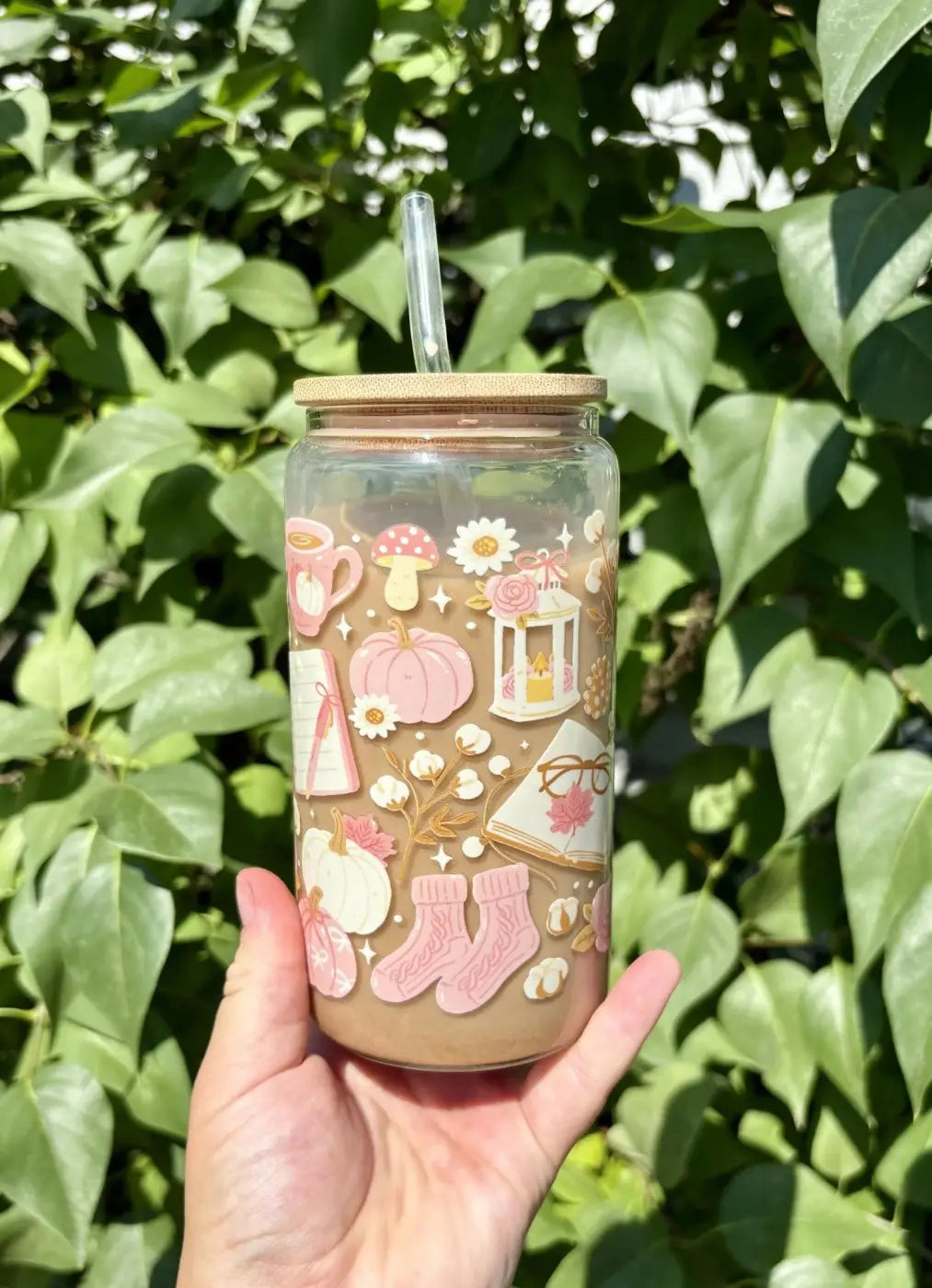 A clear glass autumn girly cup with a bamboo lid and straw decorated with pink seasonal beverage stickers