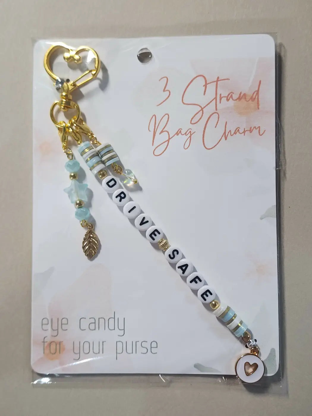 Gold-toned bag charm with drive safe letter beads, blue striped charms, gold leaf pendant, ideal for canadian made skincare gifts