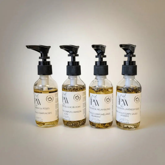 Four clear glass bottles with black pumps containing sweet almond oil, apricot oil, and jojoba oil bath and body oils labeled in english and french
