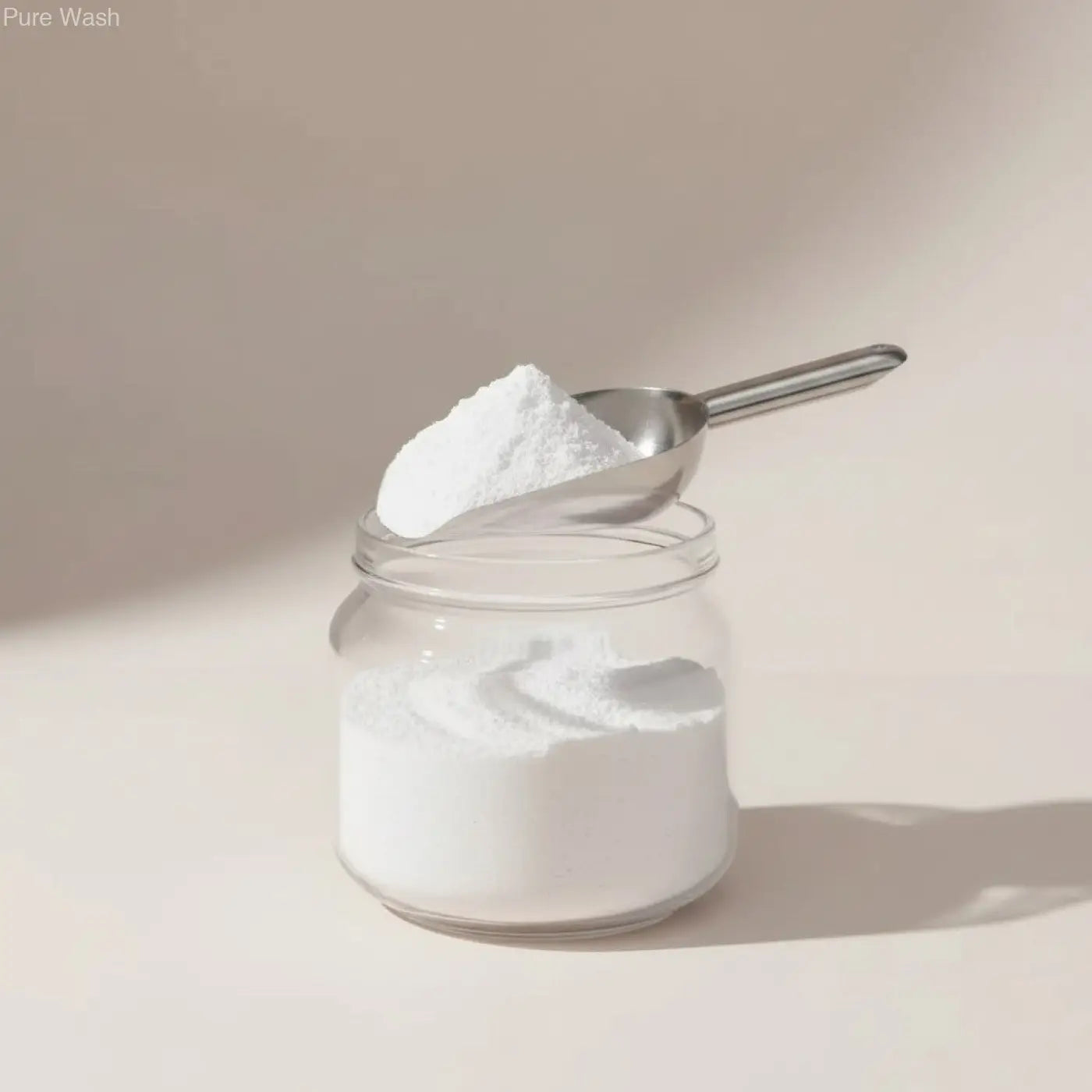 Clear glass jar filled with white bath bomb powder topped with a metal scoop highlighting nourishing oils and pure wash benefits