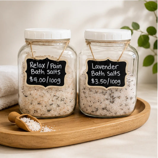 Two clear glass jars of canadian made skincare bath salts with white lids and rustic twine bows labeled relax pain and lavender