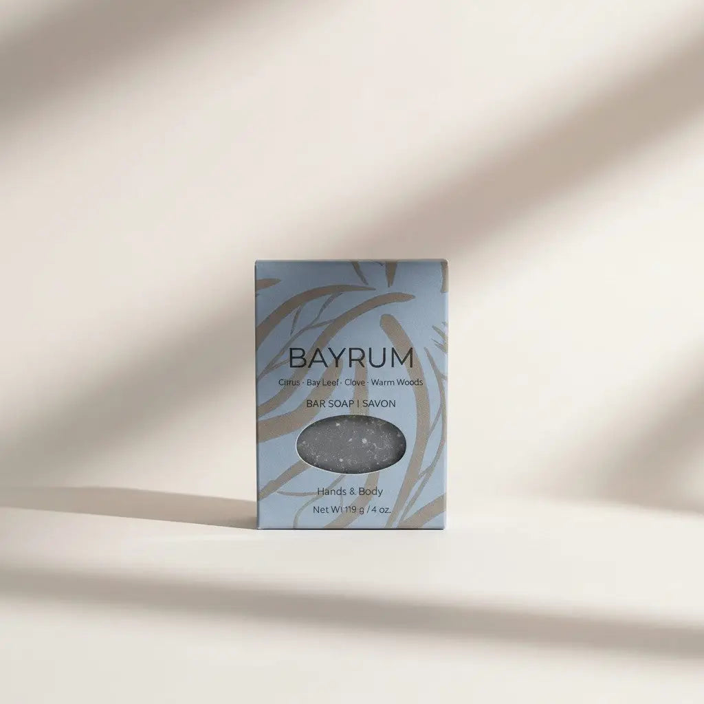 Bay rum soap bar in a light blue and beige leaf-patterned box with an oval window showing grayish sodium shea butterate soap