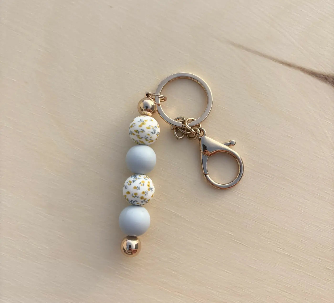 A silicone bead keychain with blue floral silicone beads, alternating matte blue and white floral patterns with gold accents