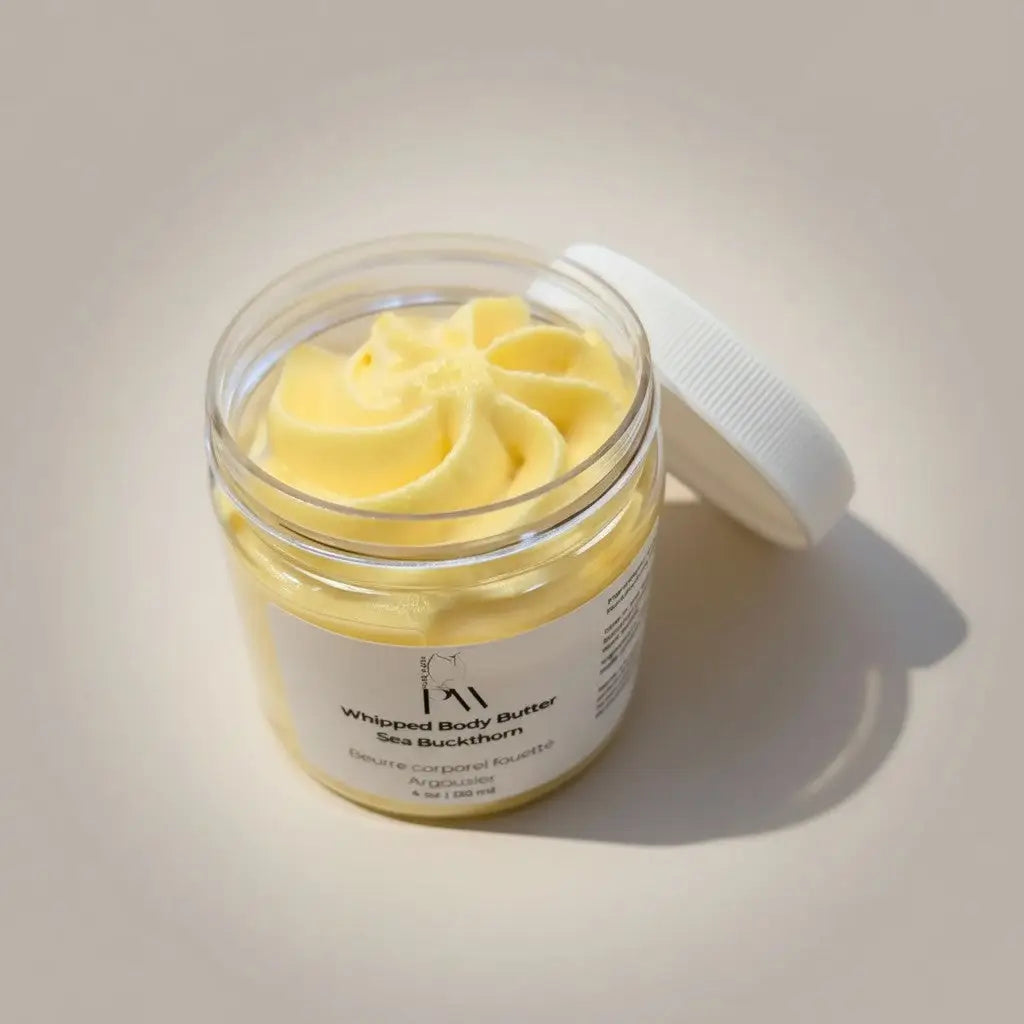 A clear glass jar of creamy yellow whipped body butter with sea buckthorn featuring cocos nucifera and theobroma cacao