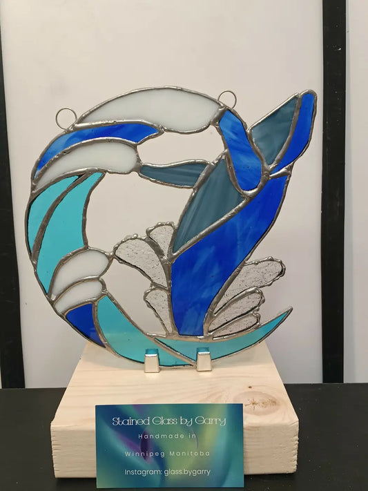 Breaching whale handmade stained glass artwork featuring a circular dolphin design in blue and teal framed by silver lead lines