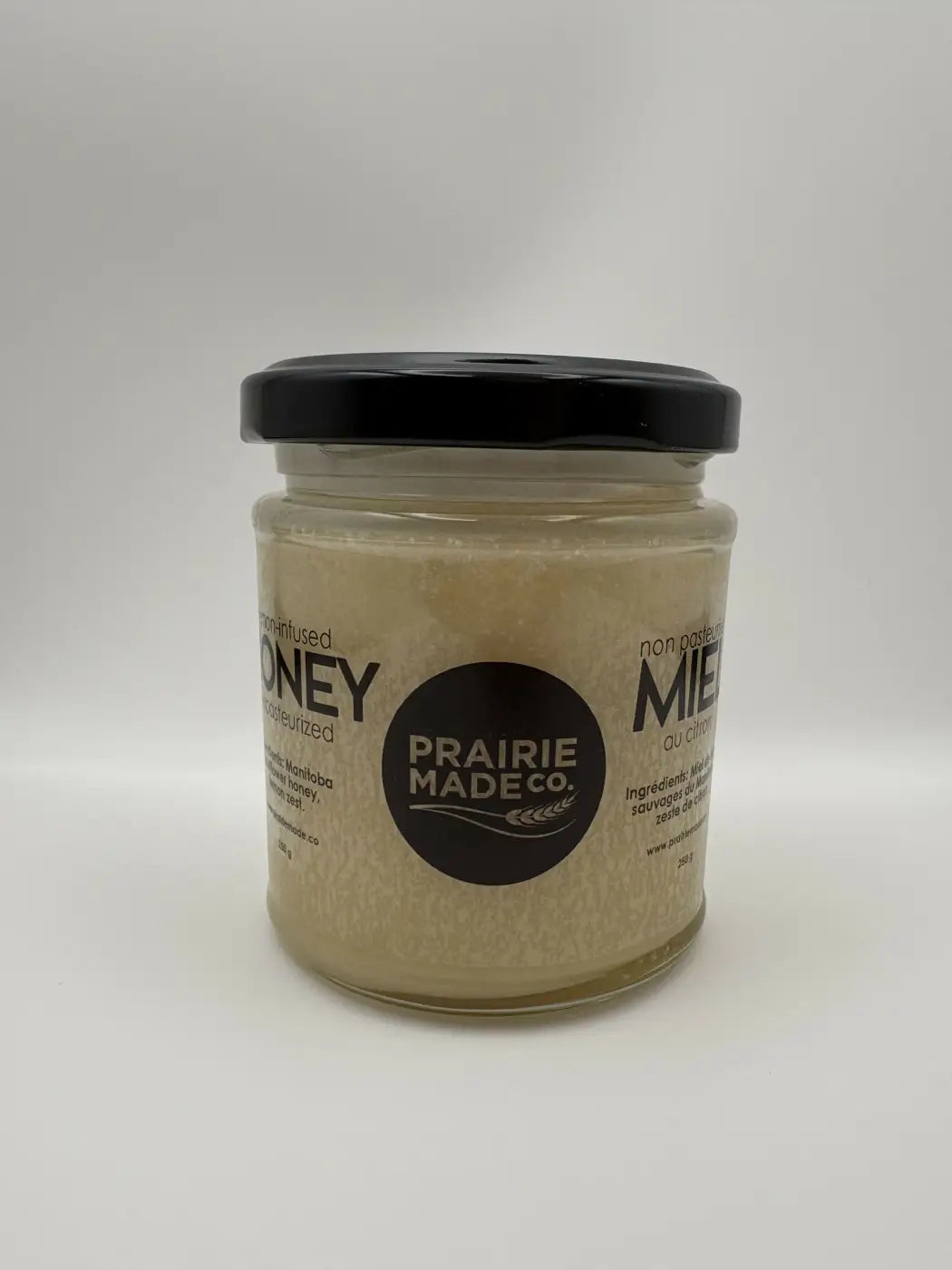 A clear glass jar with a black lid contains golden cinnamon infused honey by prairie made co for natural skincare canada