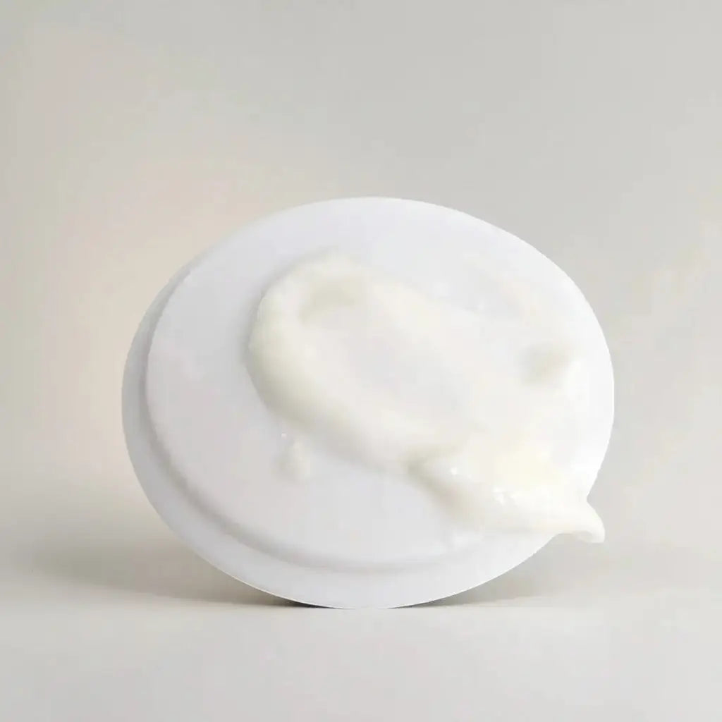 A white circular container lid with a dollop of creamy nourishing moisturizer for mature skin with shea butter