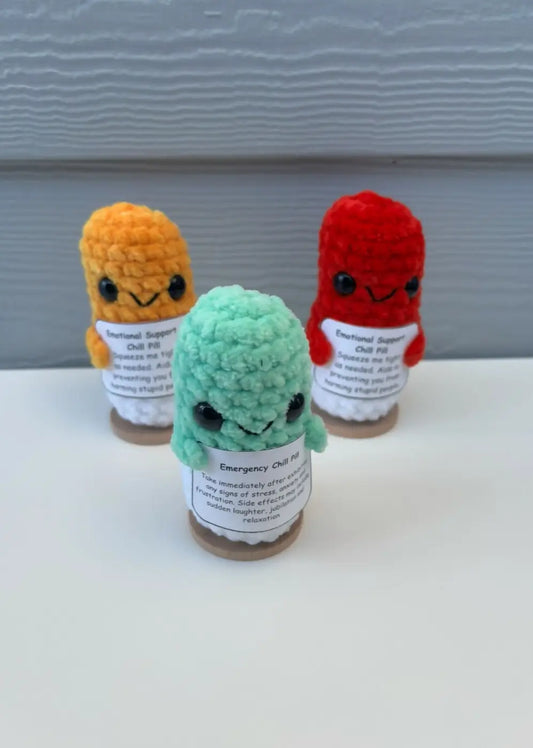 Three knitted plush emotional support chill pill figurines in orange red and mint green on glass jars with labels
