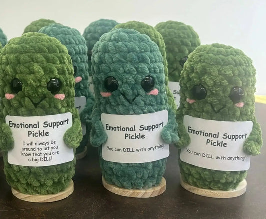 Green crocheted emotional support pickle figurines with black button eyes pink cheeks and white support pickle labels