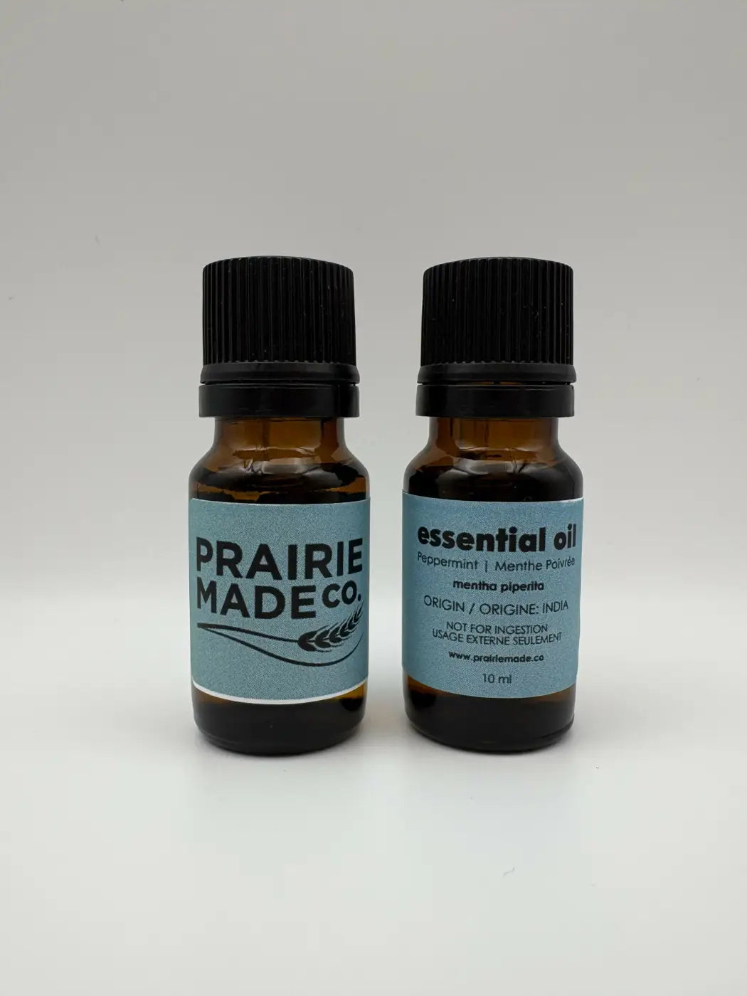 Two amber glass essential oil bottles with black caps and blue prairie made co labels for natural skincare canada
