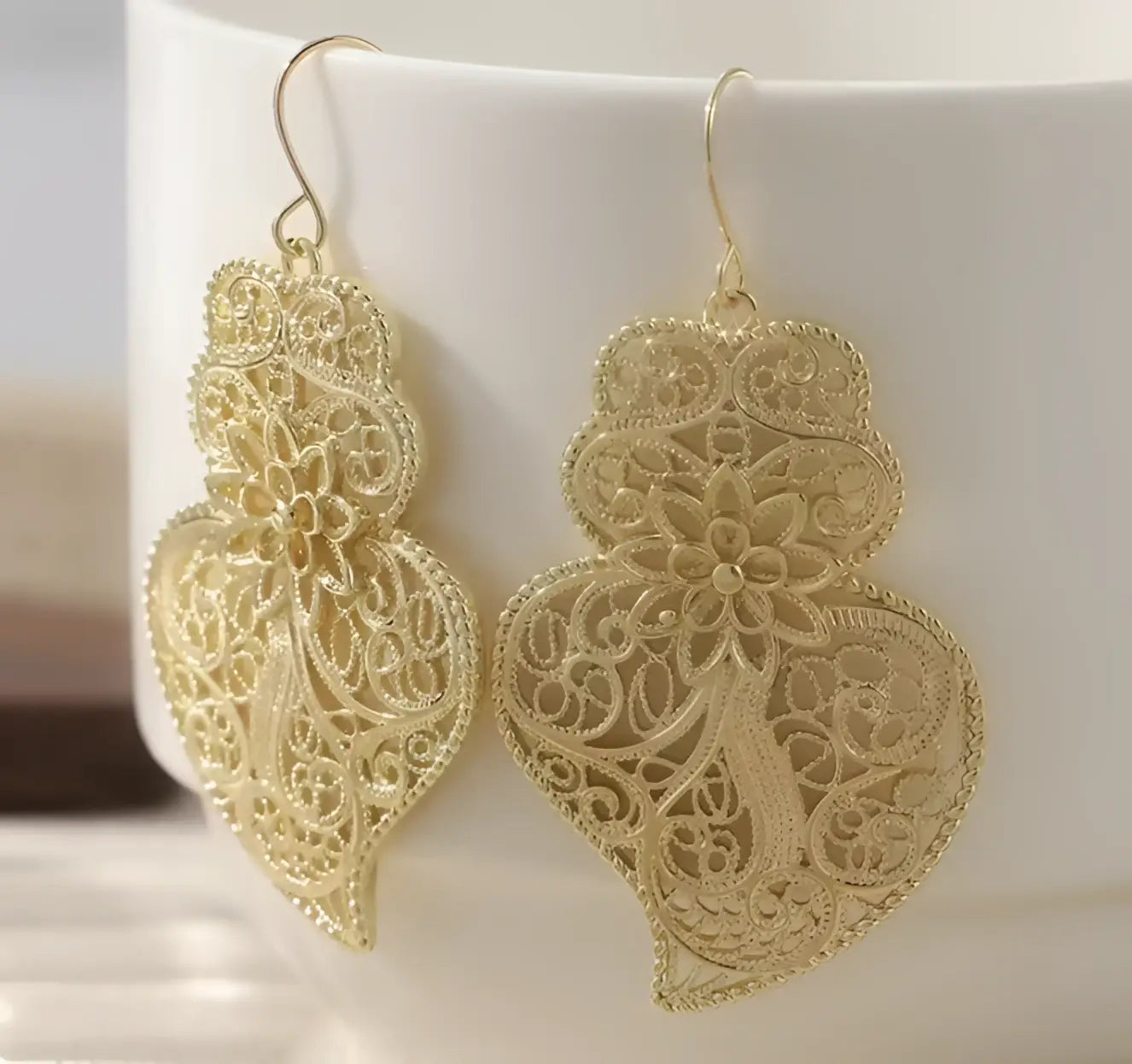Delicate gold-toned filigree earrings with intricate floral and swirling lace patterns featuring carved heart design