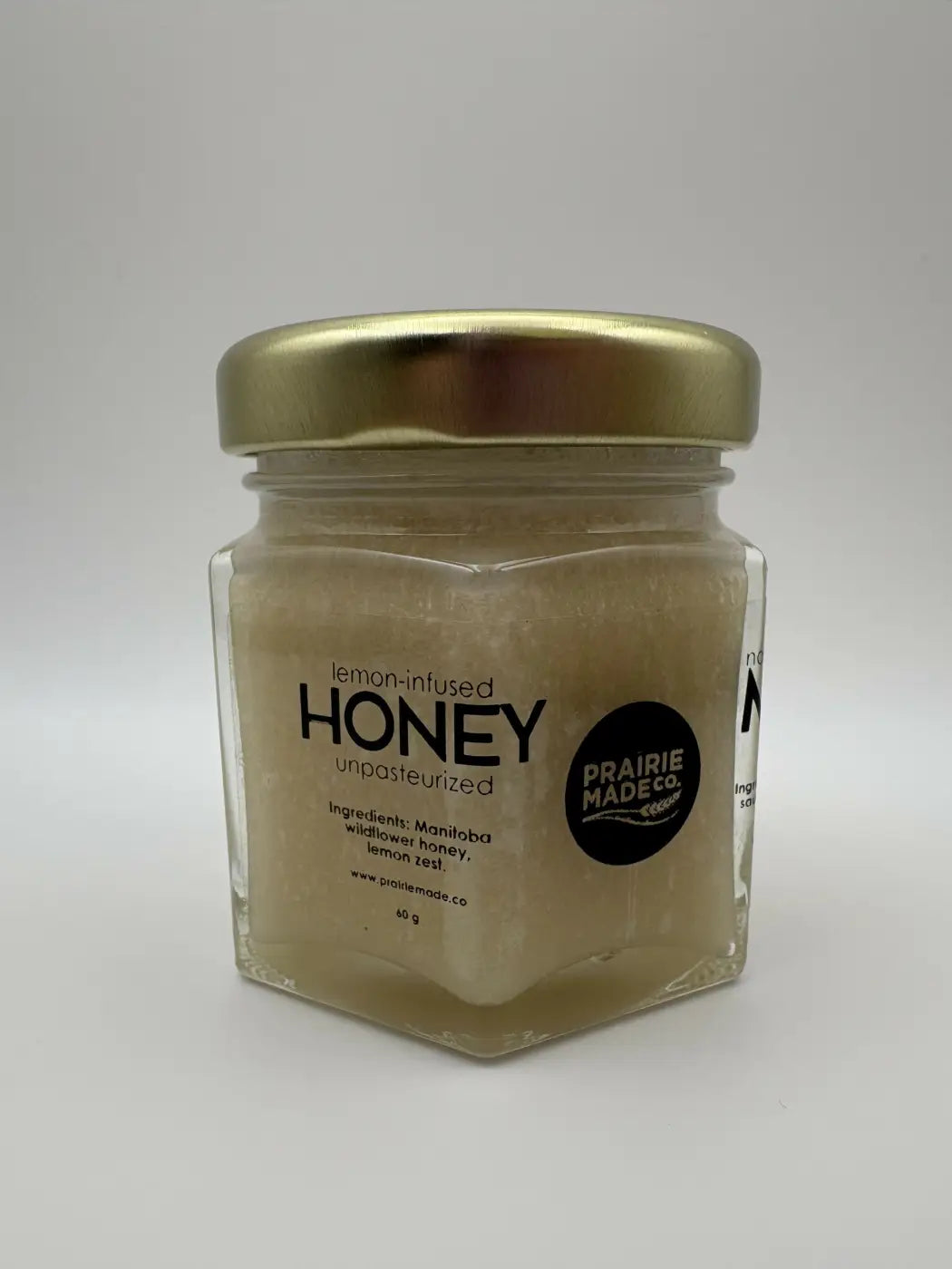 A clear hexagonal glass jar with gold lid containing unprocessed lemon-infused honey from prairie made co flavoured honey trio