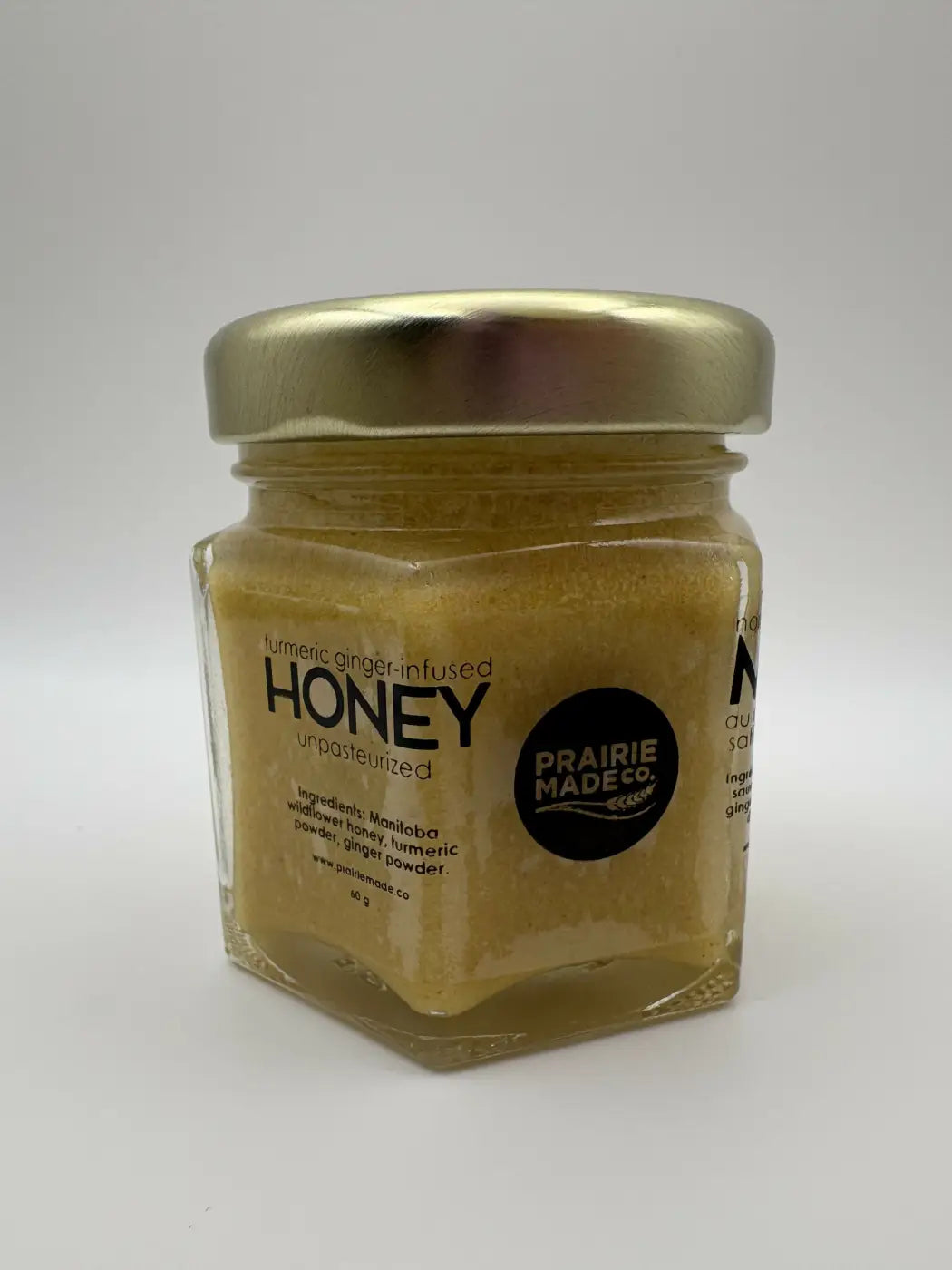 A hexagonal glass jar with a metallic lid contains golden turmeric ginger honey from prairie made co flavoured honey trio