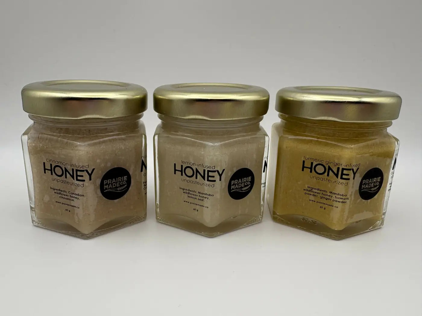 Three hexagonal glass jars with gold lids containing cinnamon, lemon, and turmeric ginger flavoured honey trio by prairie made co