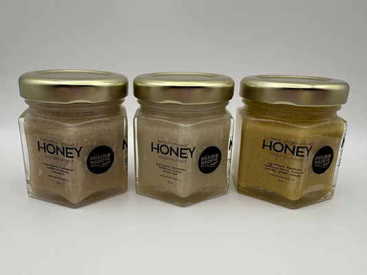 Three hexagonal glass jars with gold lids containing cinnamon, lemon, and turmeric ginger flavoured honey trio by prairie made co