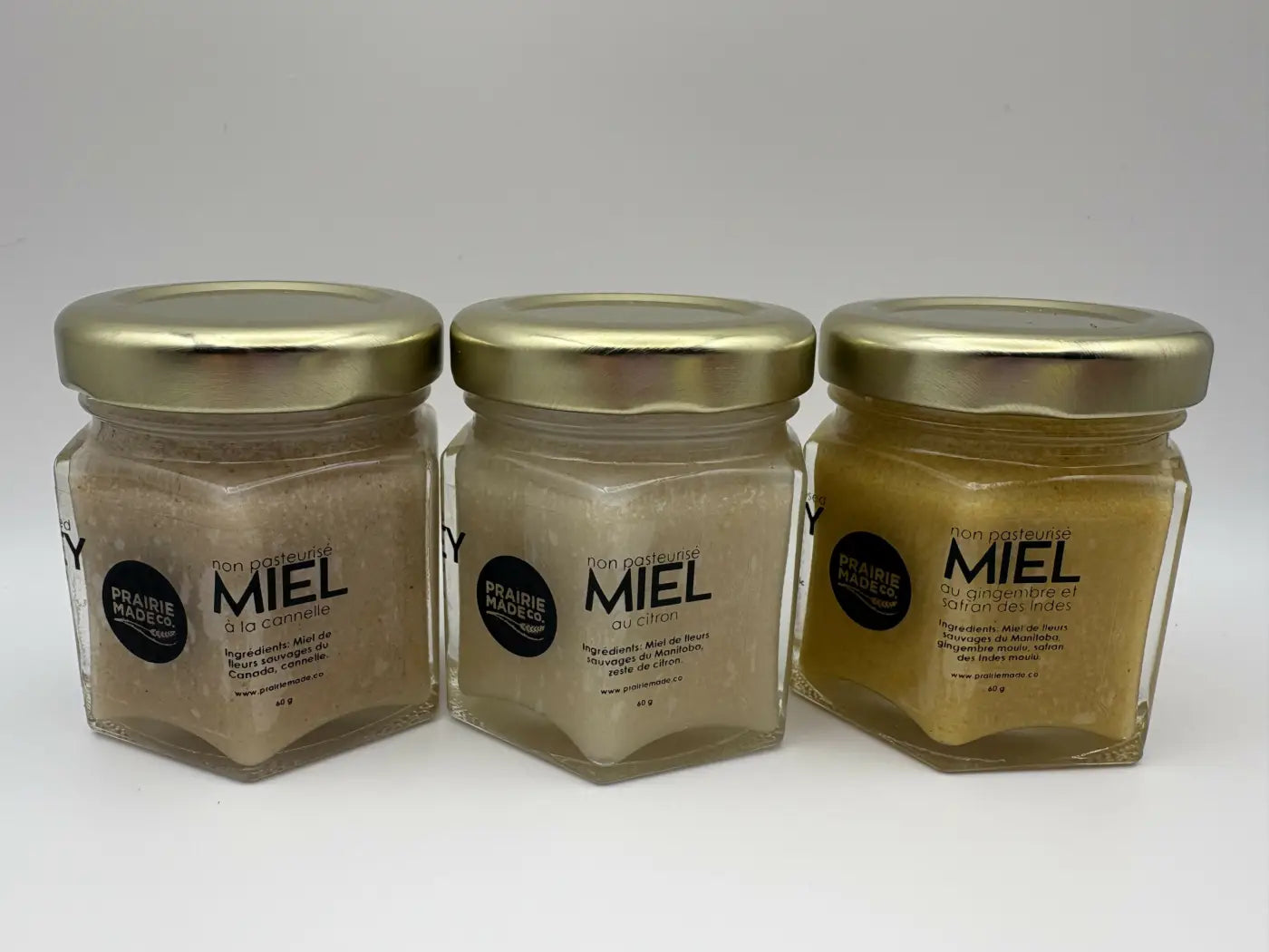 Three hexagonal glass jars with gold lids containing prairie mades flavoured honey trio including turmeric ginger