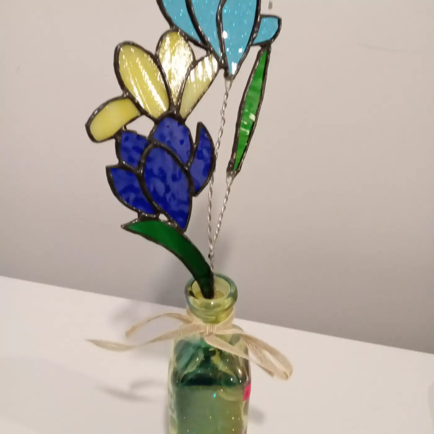 Flower grouping with stand featuring multi-colored stained glass flowers in blue yellow and green set in a clear bottle