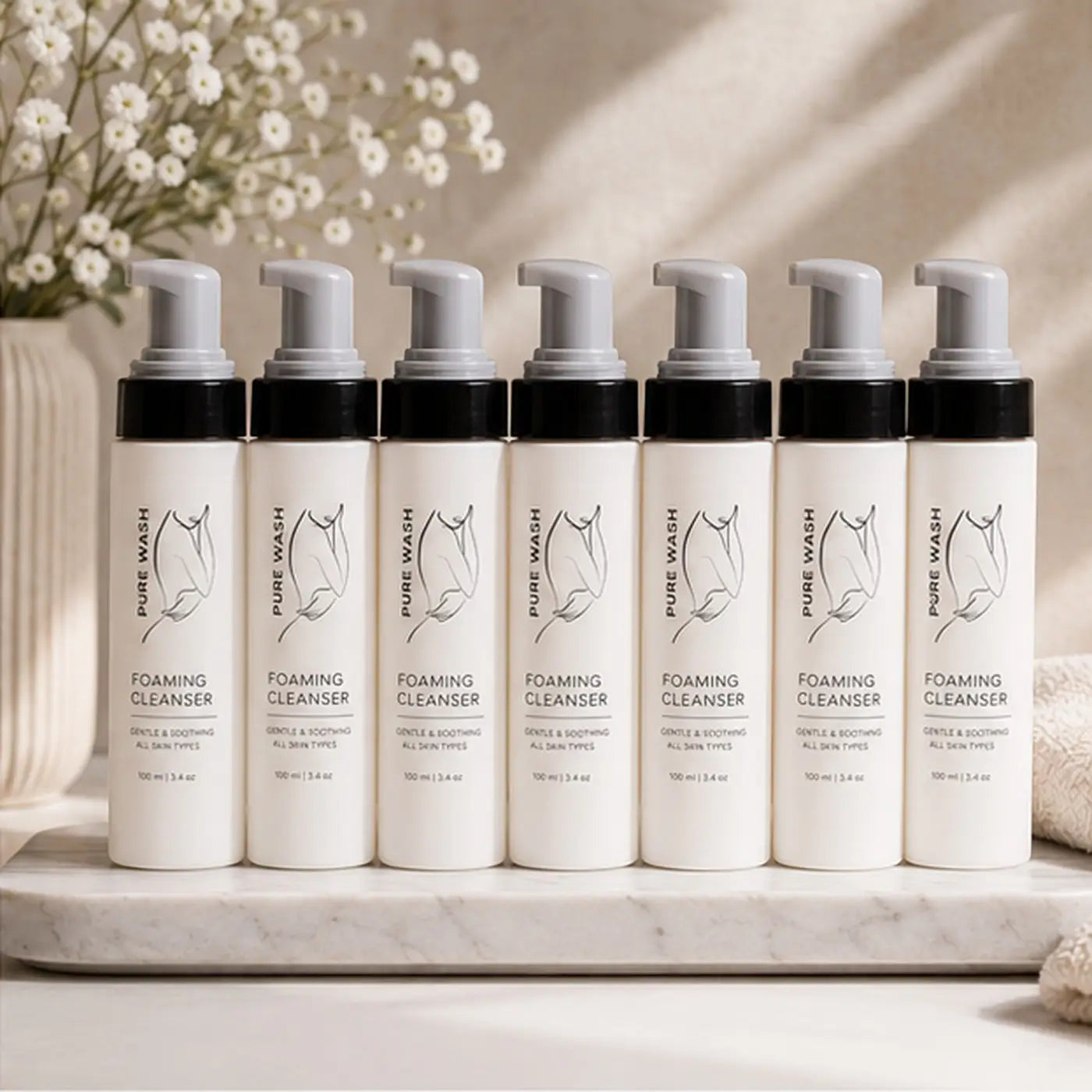 White cylindrical bottles of foaming hand soap with black pump tops and minimalist line art labels for hand cleansing