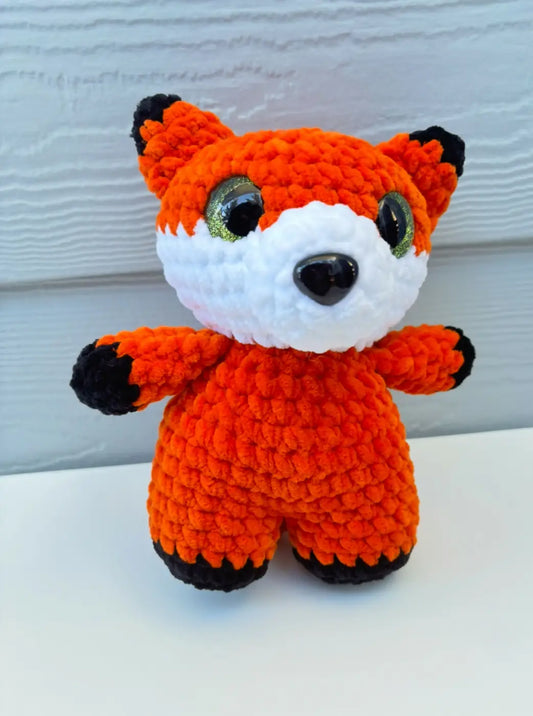 A charming orange crocheted fox plush toy with black-tipped ears and paws featuring shiny green eyes for canadian made skincare gifts