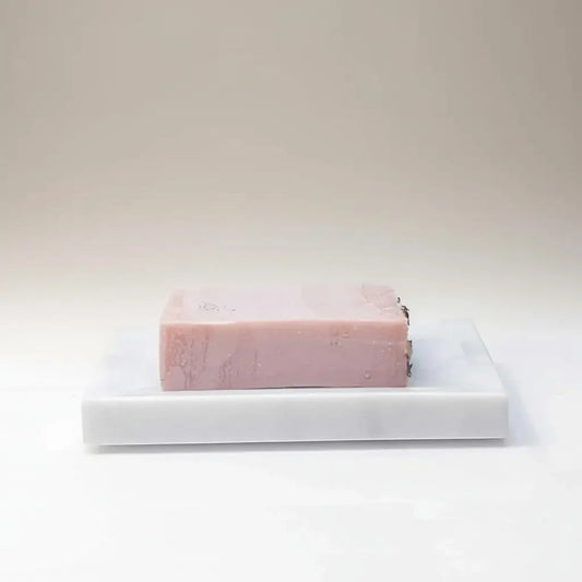 A rectangular pink fruity floral fiesta soap bar with subtle marbling on a white marble soap dish by rocky mountain soap