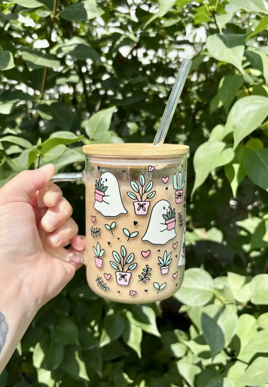 A clear glass plants mug with bamboo lid and handle featuring pastel ghost and plant illustrations with glass straw