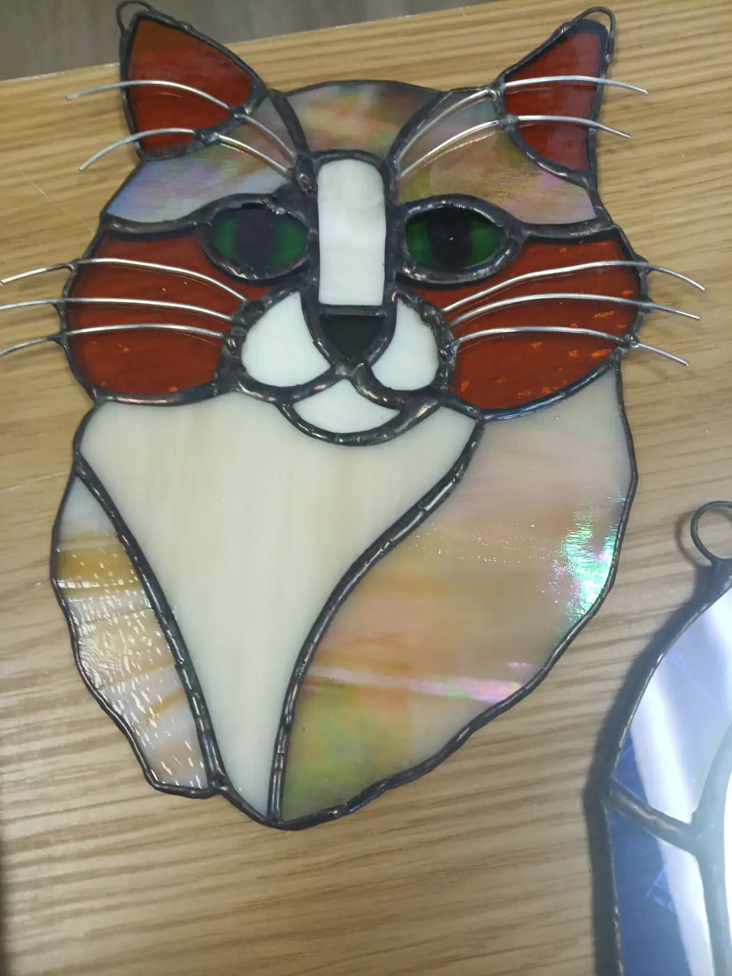 A stained glass cat headshot with green eyes in red white and green hues set in a leaded frame