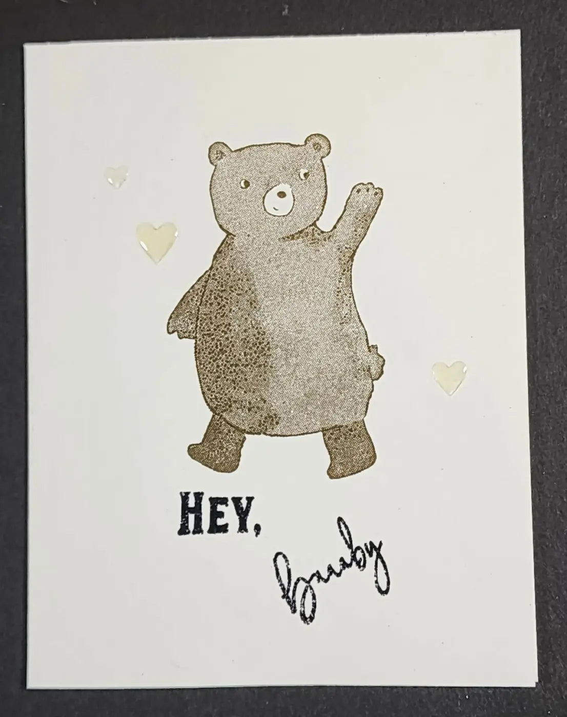 A charming brown bear illustration greeting card on white card waving surrounded by translucent hearts natural skincare canada