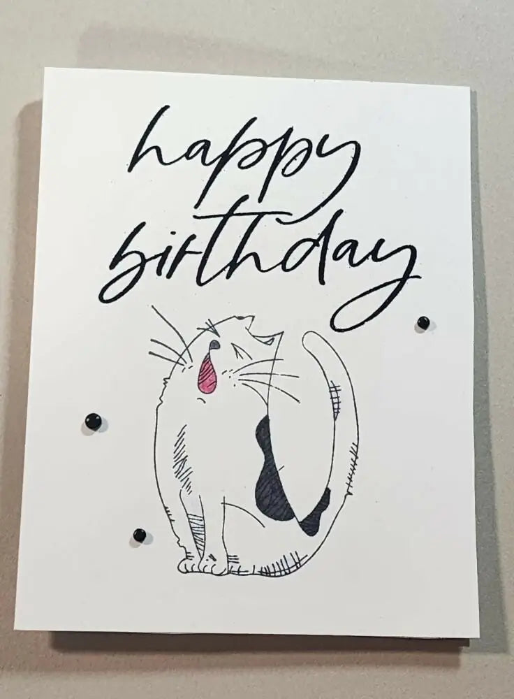 A white greeting card with a black ink cat sketch, pink tongue, and three small black beads, ideal for natural skincare Canada gifts