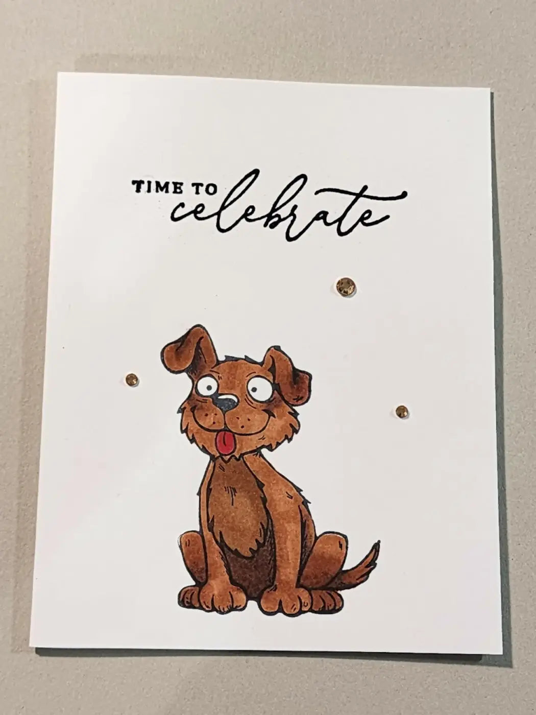 A charming brown illustrated puppy sits on a white greeting card with time to celebrate for natural skincare Canada
