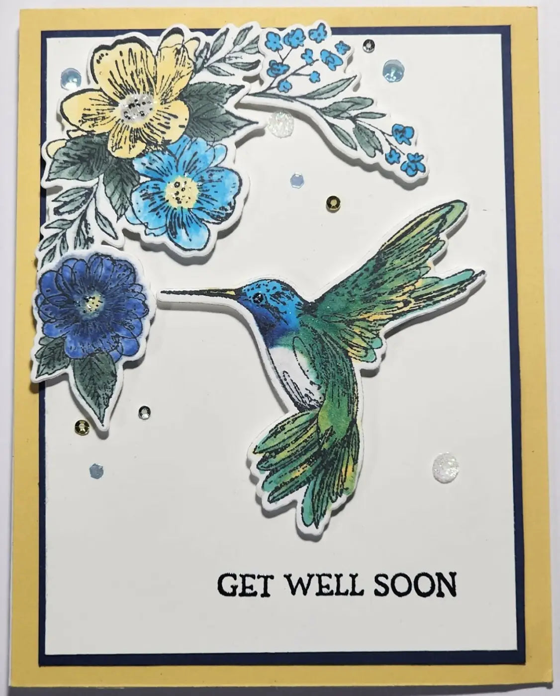 Colorful handcrafted greeting card featuring a detailed blue and green hummingbird with yellow and blue floral designs Canadian made skincare