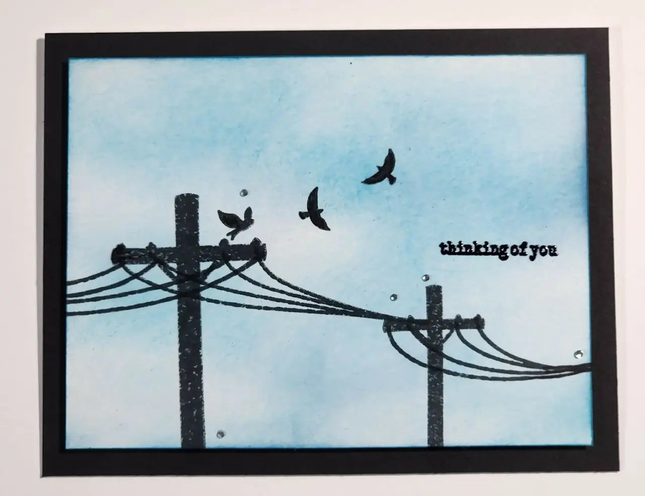 Black-framed handmade greeting card featuring bird and power line silhouettes on blue background with thinking of you text