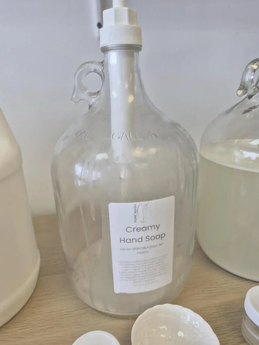 Clear glass jug with white pump dispenser labeled pure wash creamy hand soap for premium hand soap with natural ingredients